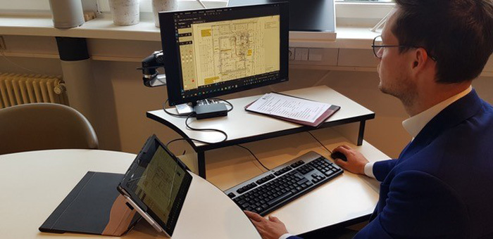 man wearing suit and glasses looking at construction blueprints on computer in office 