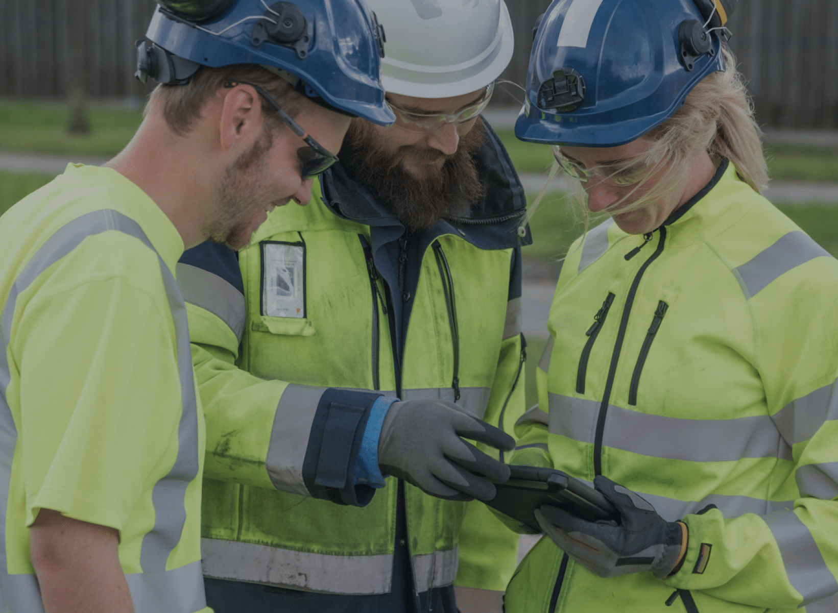 Three construction workers consult a tablet computer on-site