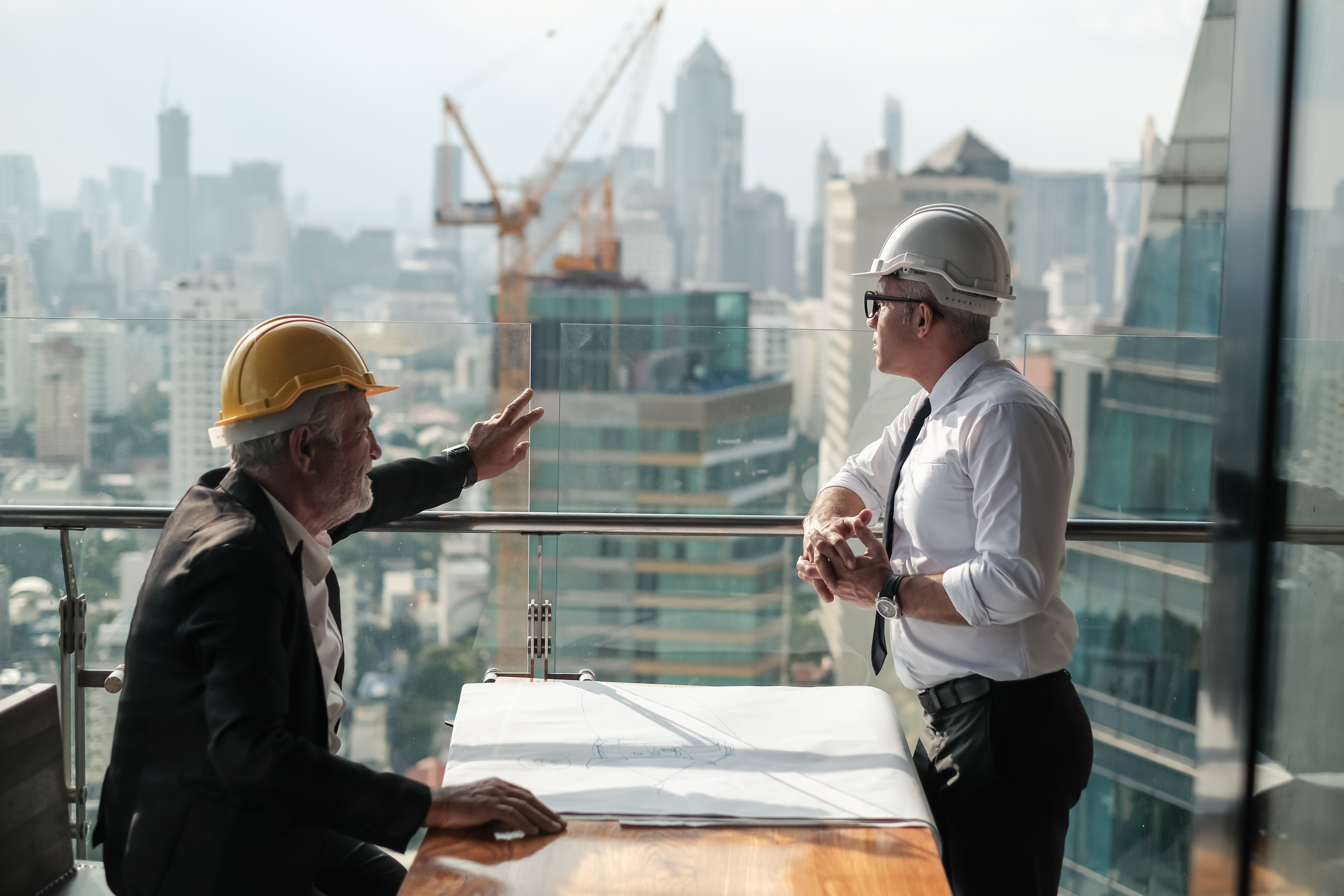 Two architects examine plan while looking out at skyscrapers