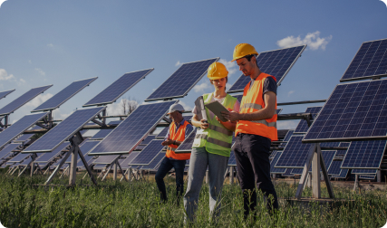 Construction workers in safety gear look at iPad together in front of solar panels