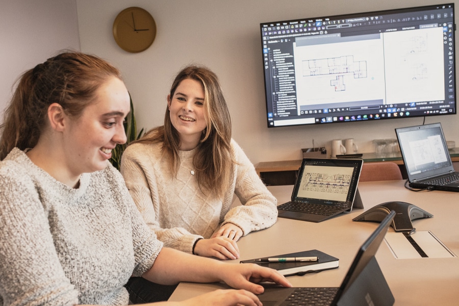 two women working on laptops with construction drawings on screens in the background