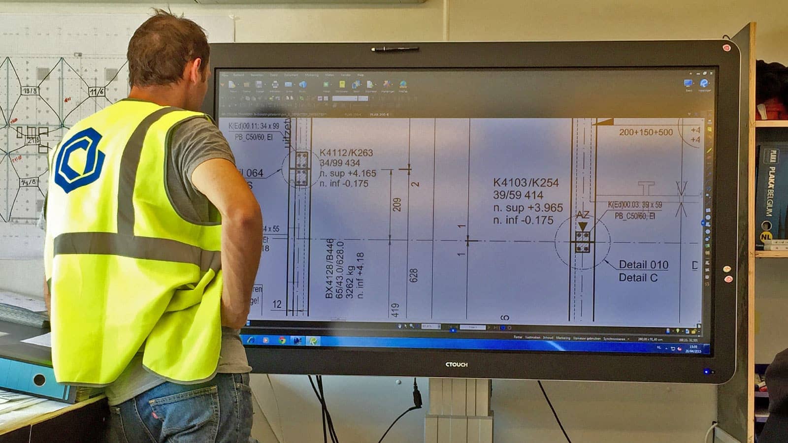 Man in PPE looking at construction drawing on big screen