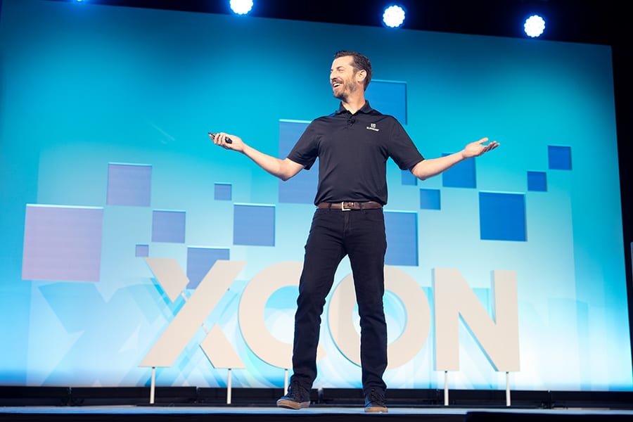 Andrew Gaer smiles as he speaks on-stage at XCON