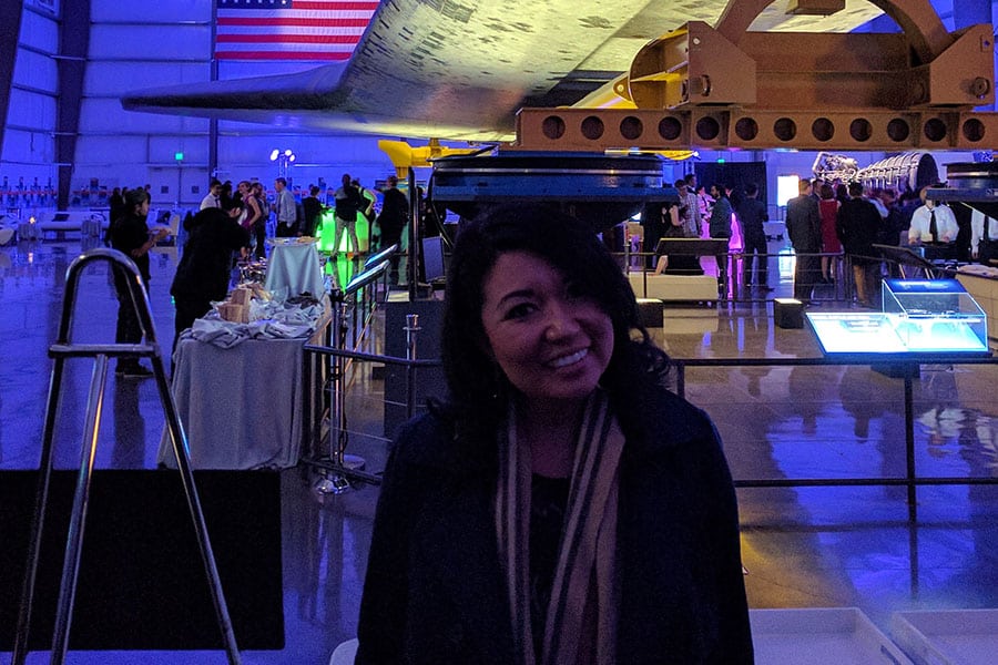 Erika Saniano smiles underneath a space shuttle at a Bluebeam party