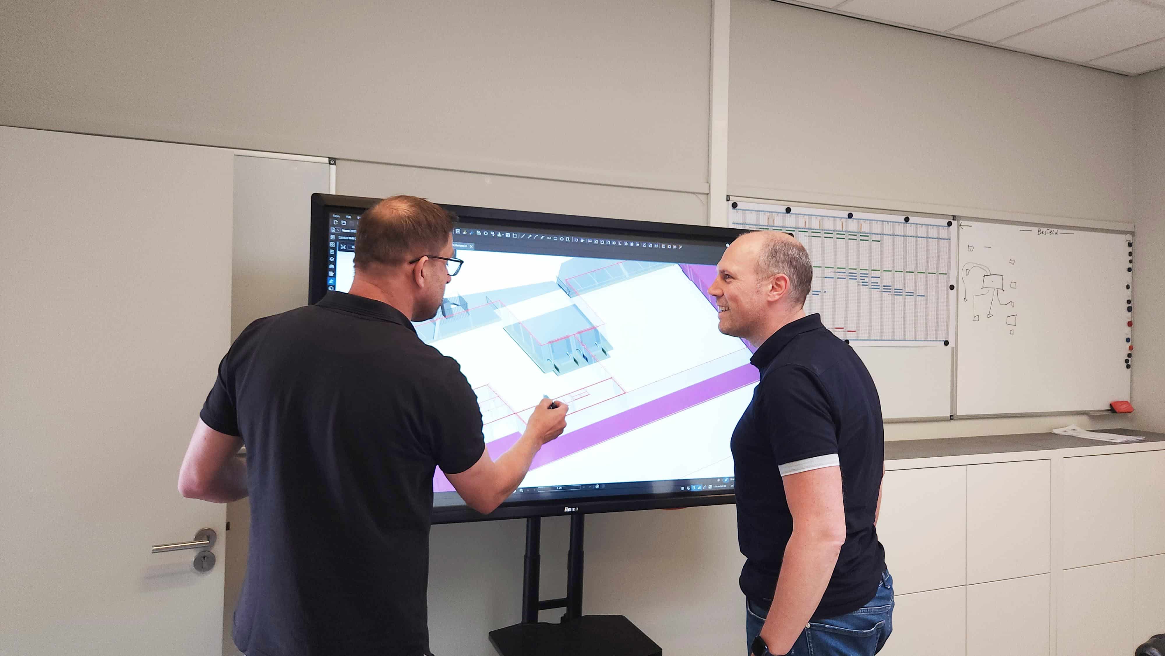 Two SMG employees discuss a PDF in Revu, shown on a TV screen