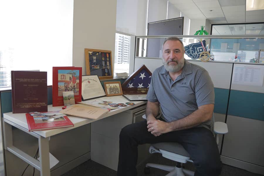 Ernesto Obregon, senior enterprise and international support manager, sits next to a desk showcasing his military medals, awards, and other memorabilia.