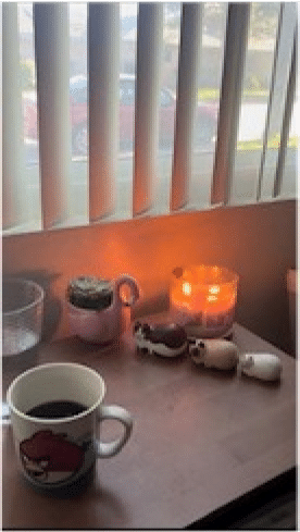A picture of Vivien's desk, with a coffee mug, a glass of water, a candle, and three small cat decorations.