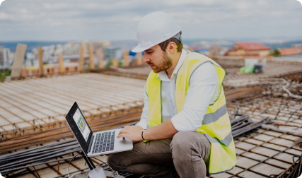 Construction worker on roof crouches down with laptop
