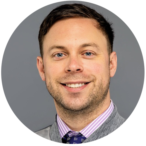 Smiling man with short brown hair and blue eyes, wearing a grey jacket, purple striped shirt, and patterned tie, pictured against a plain gray background—perfect for showcasing the professional behind your construction management software.