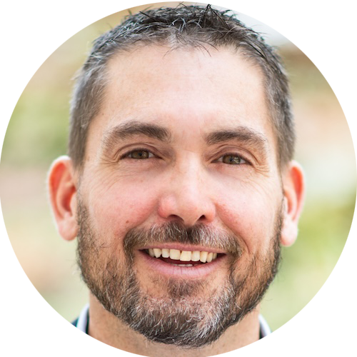 A close-up portrait of a smiling man with short dark hair, a trimmed beard, and mustache, against a softly blurred outdoor background—perfect for showcasing professionals who rely on contractor software or construction estimating software.