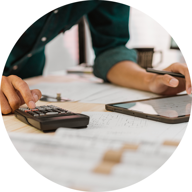 A person uses a calculator and tablet on a desk filled with papers and charts, suggesting they are working on financial calculations or analyzing data for Construction Takeoffs.