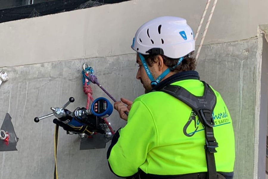 Construction worker inspects a device attached to the wall and his harness.